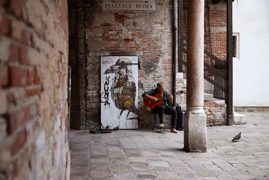 Man playing guitar in Venice, Italy with birds around him