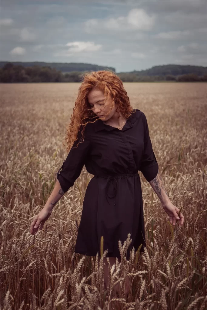 Portrait of a red-haired woman who's standing in a wheat field looking down