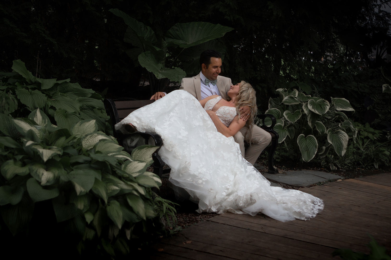 a newly wed couple on a park bench surrounded by hostas